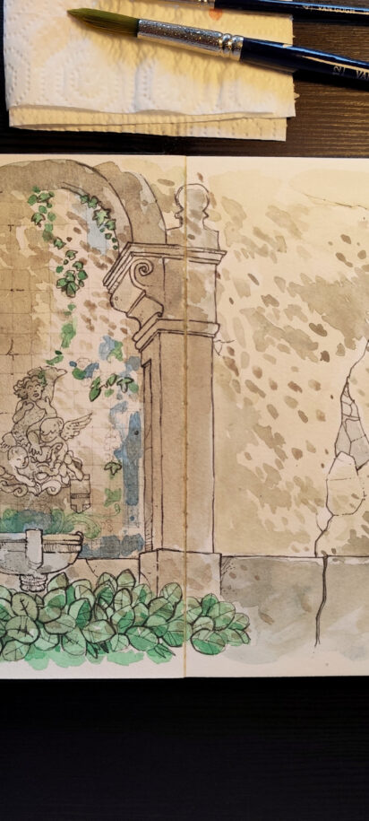 A imagem mostra uma mesa de trabalho vista de cima, com um caderno aberto exibindo uma ilustração feita em aquarela e caneta. A ilustração retrata uma estrutura antiga de pedra, semelhante a uma fonte ou nicho decorativo. No centro há uma pequena escultura de figura humana clássica, cercada por blocos de pedra irregulares e trepadeiras verdes que descem suavemente pelas laterais do arco. Na base, uma bacia de pedra e folhagens amplas em tons de verde reforçam a sensação de um jardim antigo e silencioso. O conjunto transmite uma atmosfera tranquila e contemplativa, evocando a passagem do tempo sobre a arquitetura. Ao redor do caderno, sobre a mesa escura, há materiais de pintura: à esquerda, uma paleta de aquarela usada com cores misturadas; acima, um frasco translúcido de vidro, pincéis apoiados sobre um papel toalha; à direita, três canetas de desenho. A luz é suave e quente, iluminando principalmente o centro do caderno, criando um ambiente de trabalho calmo e íntimo, como um momento de estudo artístico dedicado e sereno.